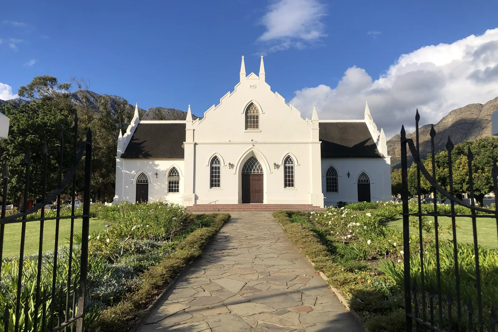 A white gabled church at the end of a garden path, mountains behind